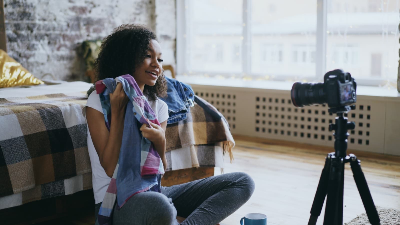 Woman recording a video with a camera on a tripod in a bright bedroom while creating content