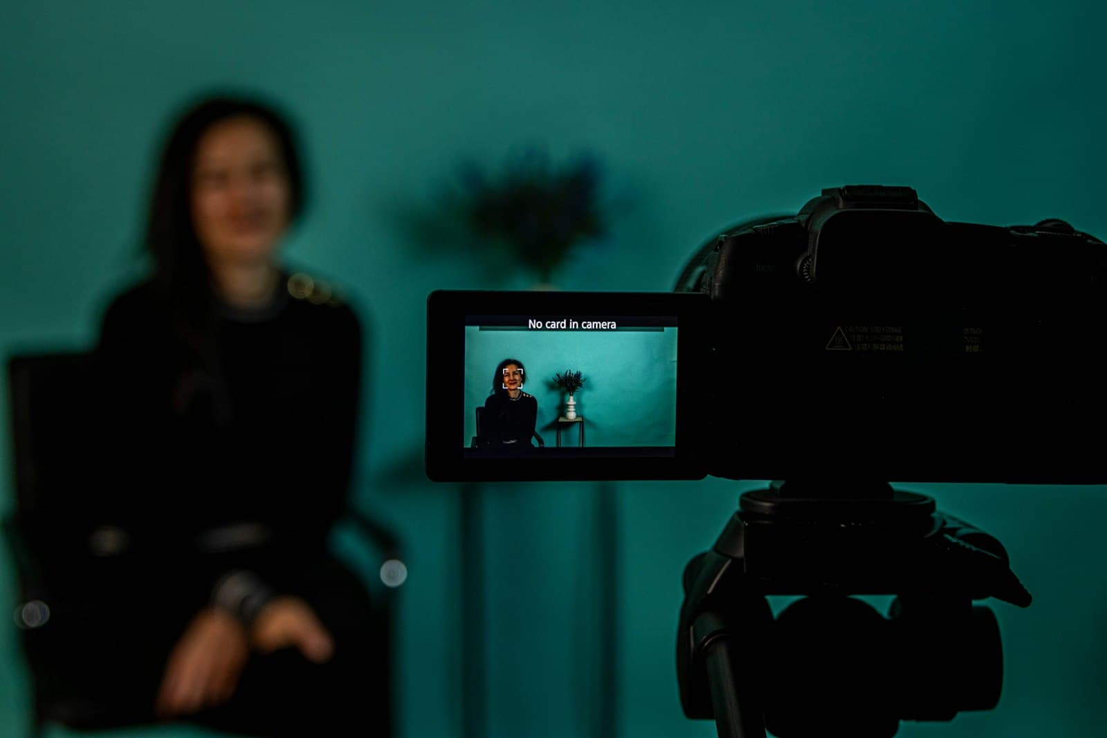 Woman being filmed for a video by a camera on a tripod in a teal-lit studio